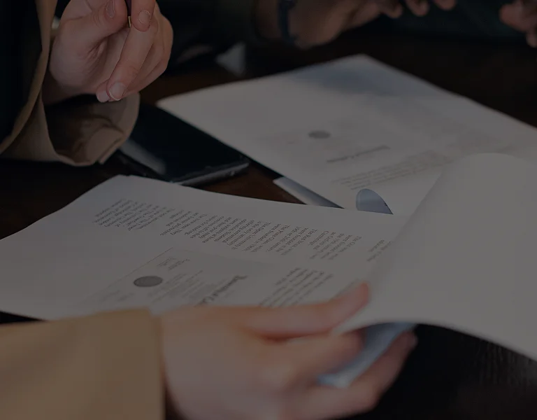 Hands of two individuals reviewing printed documents on a dark wooden table.