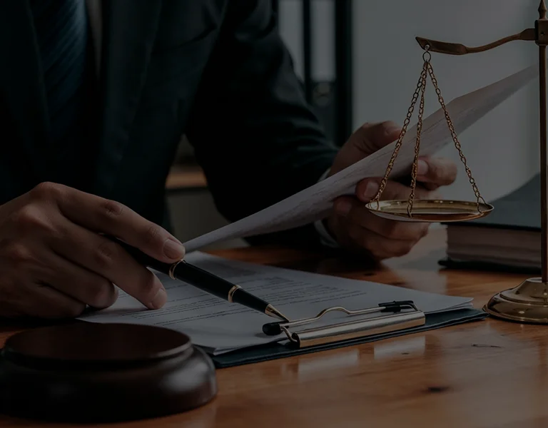 Person in dark suit reviewing documents at a wooden desk with scales of justice and gavel.