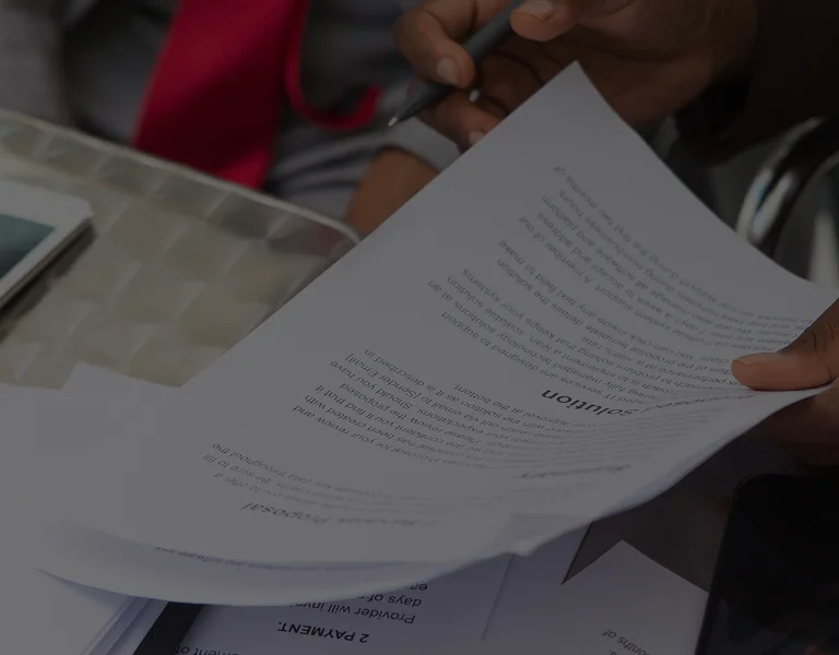 Person holding and reviewing printed documents with visible headings and text, pen in hand.