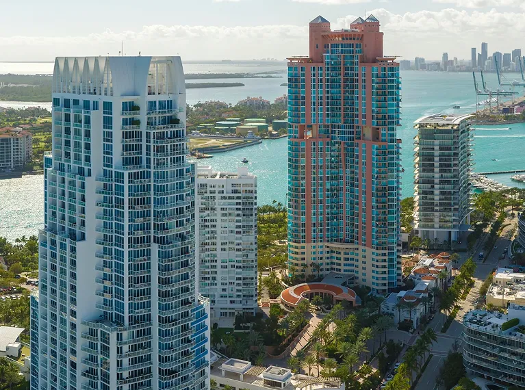 Aerial view of modern high-rise buildings near a waterfront with a city skyline in the background.
