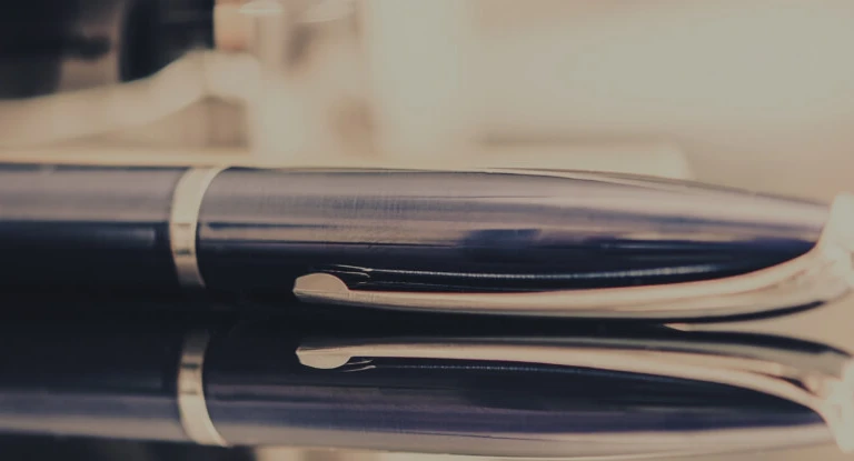 Close-up of a black and silver fountain pen resting on a reflective surface.