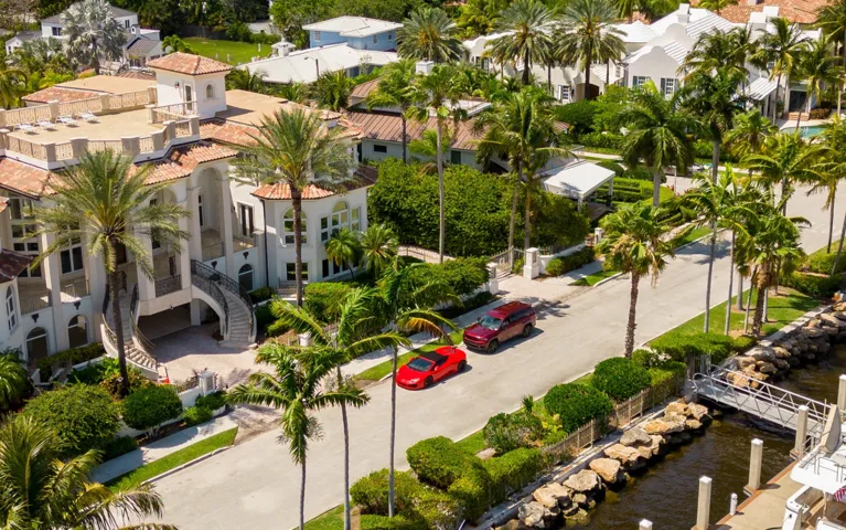 Aerial view of a residential street with luxury houses, palm trees, and two parked cars.