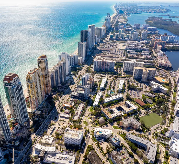 Aerial view of a coastal city with high-rise buildings along the shoreline and residential areas inland.