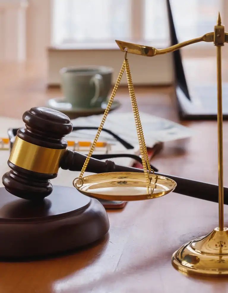 Close-up of a wooden judge's gavel and golden balance scale on a desk.