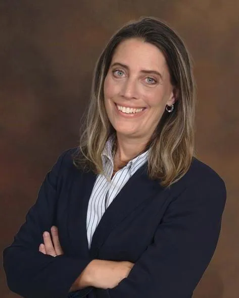 Professional portrait of a smiling woman with crossed arms, wearing a navy blazer and striped shirt.