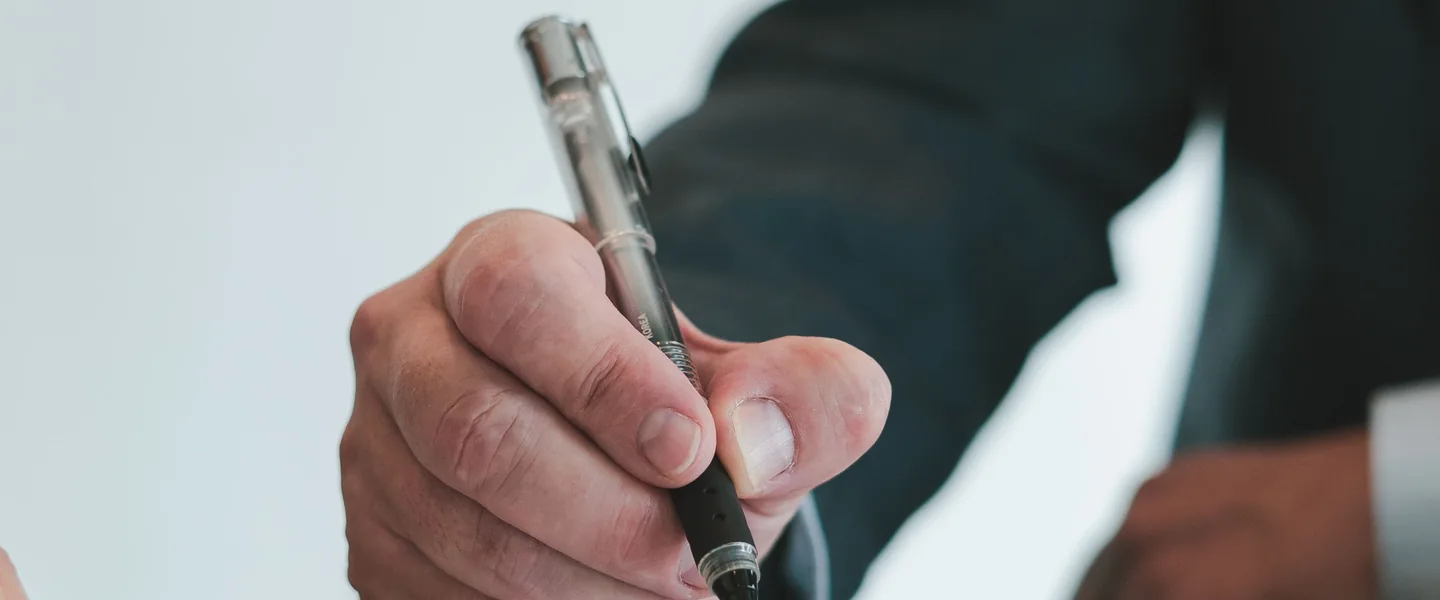 Close-up of a hand holding a black pen, poised to write on a white surface.
